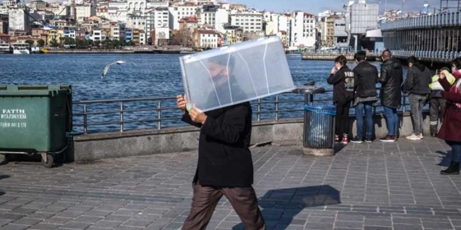 رجل يرتدي قناعًا للوجه ويحمل صندوقًا بلاستيكيا خشية الإصابة بفيروس كورونا (الأوروبية)