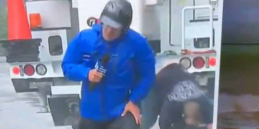 يظهر المراسل وهو يقاوم الرياح بشدة إلا أن رجلاً ظهر خلفه